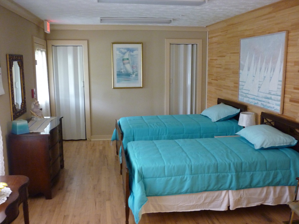 A cozy bedroom with twin beds covered in blue bedding, featuring a wooden floor and a dresser next to the entrance.