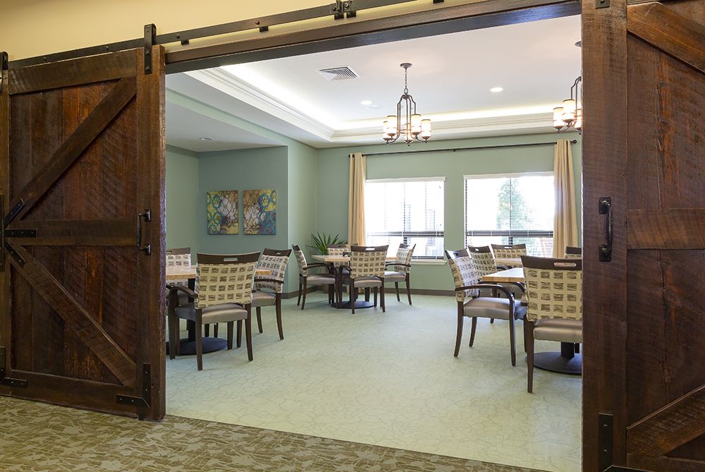 A well-lit dining room with tables and chairs arranged neatly under chandeliers.
