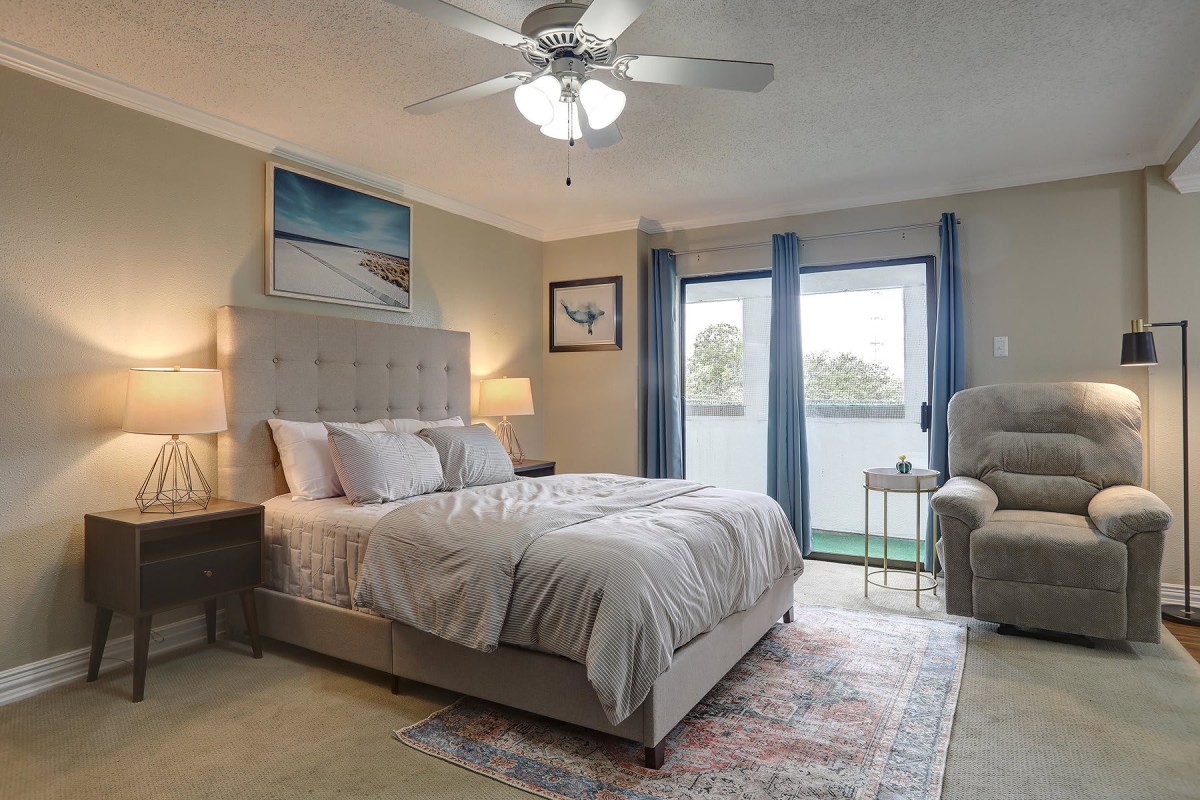A cozy bedroom featuring a comfortable bed, elegant lamps, and floor-to-ceiling windows with blue curtains.