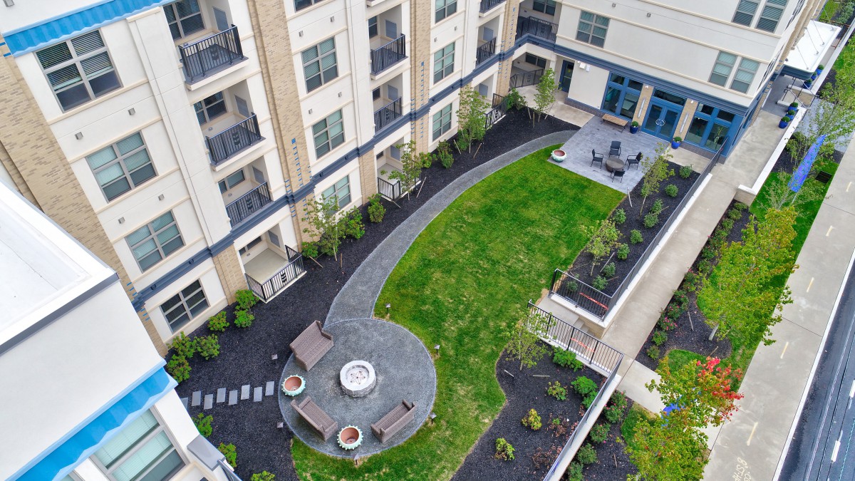 Aerial view of a modern apartment complex courtyard featuring a green lawn and patio area with a fire pit.