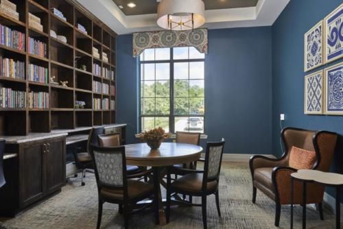 A cozy study room with a round table, chairs, and bookshelves against a blue accented wall.