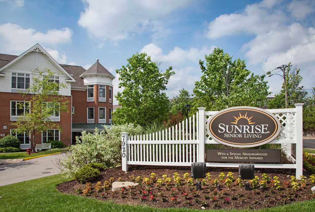 A view of a retirement community with well-maintained landscaping and a prominent entrance sign under a blue sky.