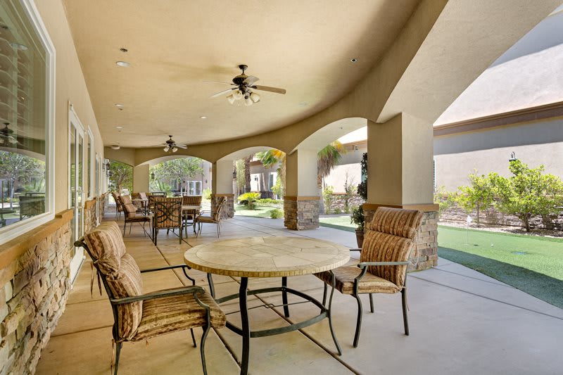 A spacious patio with wicker furniture overlooks a garden, featuring a ceiling fan for comfort.