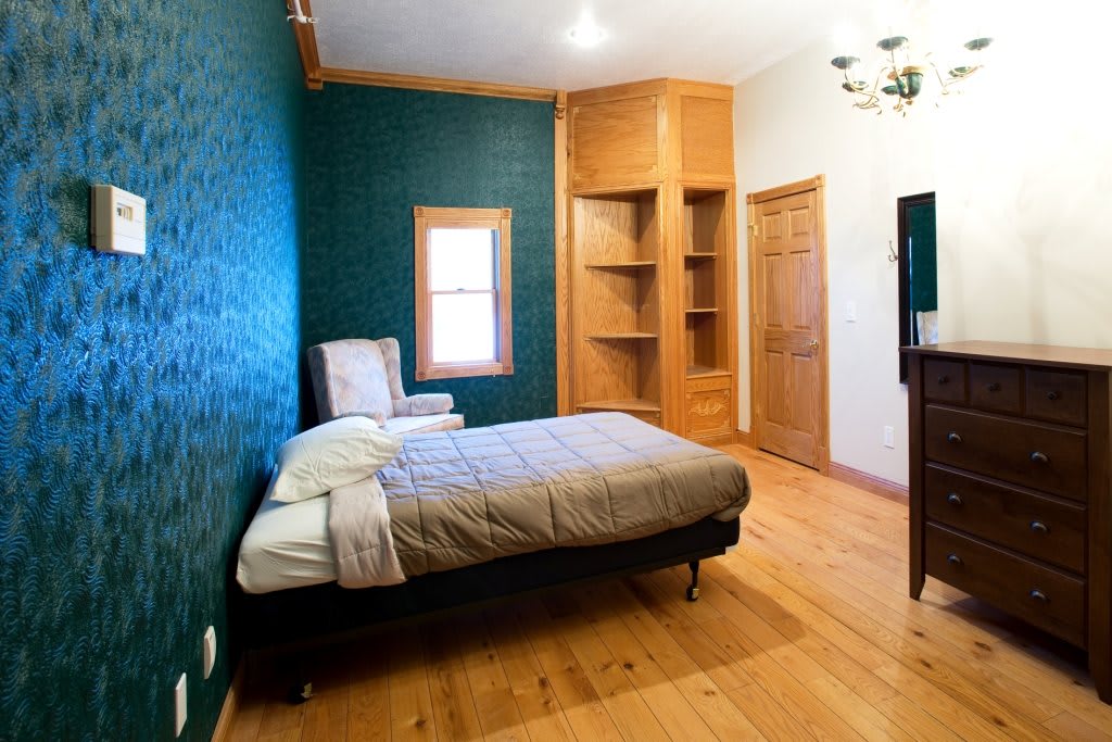 A cozy bedroom with a bed, wooden flooring, and built-in bookshelves.