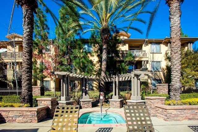 Sunny courtyard with a fountain and lounge chairs surrounded by lush greenery.