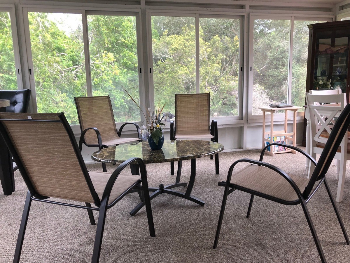 A cozy sunroom with patio furniture and a serene nature view through large windows.