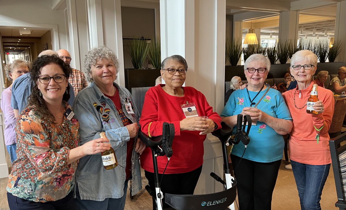 A group of seniors gather together indoors, smiling and enjoying each other's company.