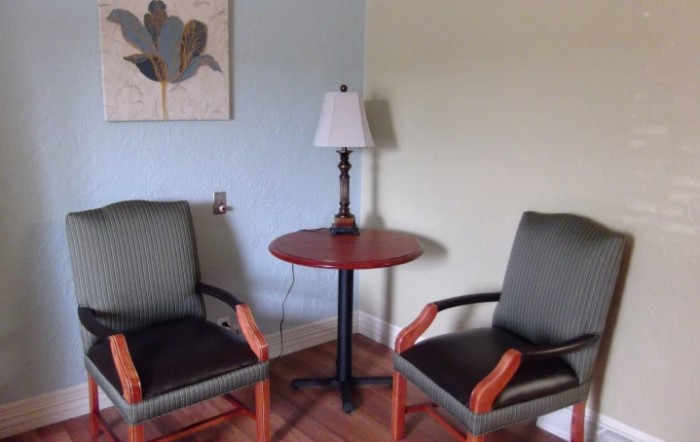 A cozy seating area with two chairs and a table, adorned by a lamp and a wall painting.