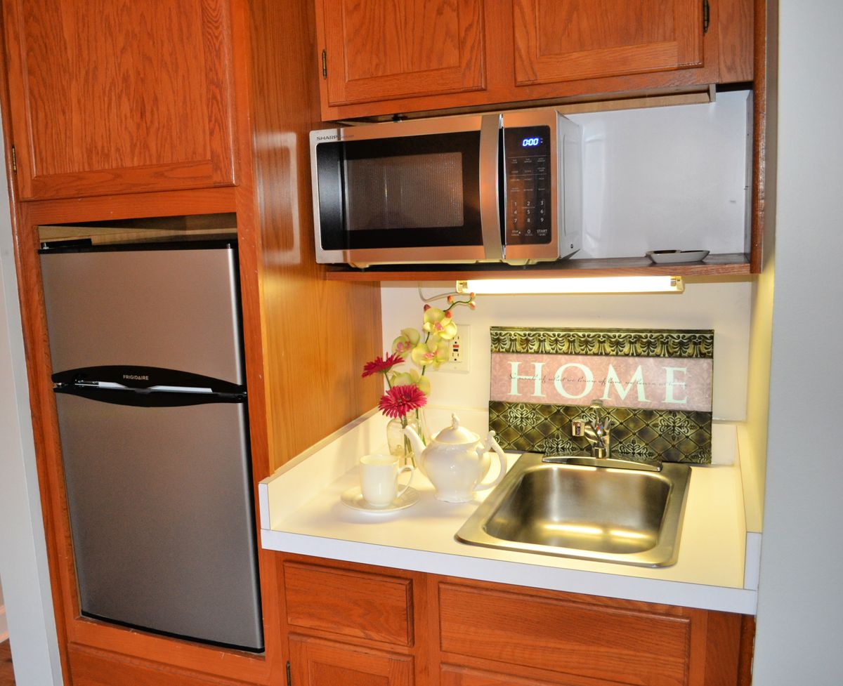 A cozy kitchen setup featuring a microwave, sink, and fridge with wooden cabinets.