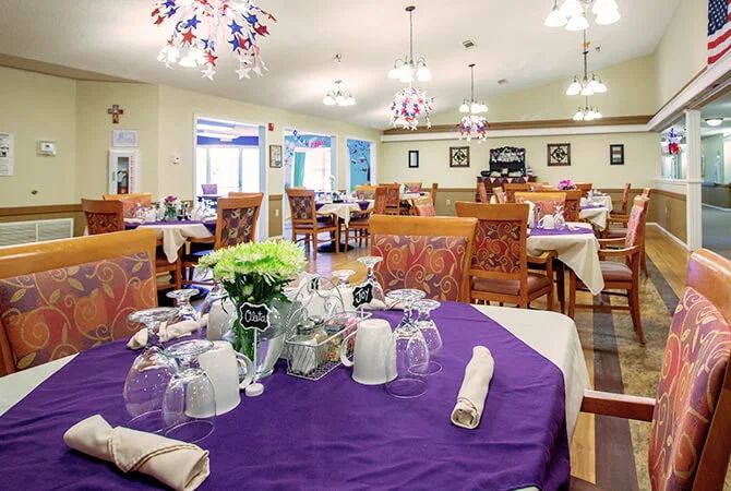 A well-decorated dining room with neatly arranged tables and chairs, featuring purple tablecloths and elegant lighting.