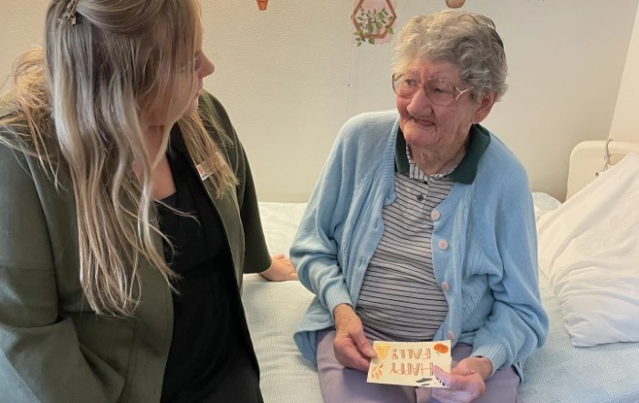 An elderly woman holding a card smiles warmly while sitting next to a younger woman.
