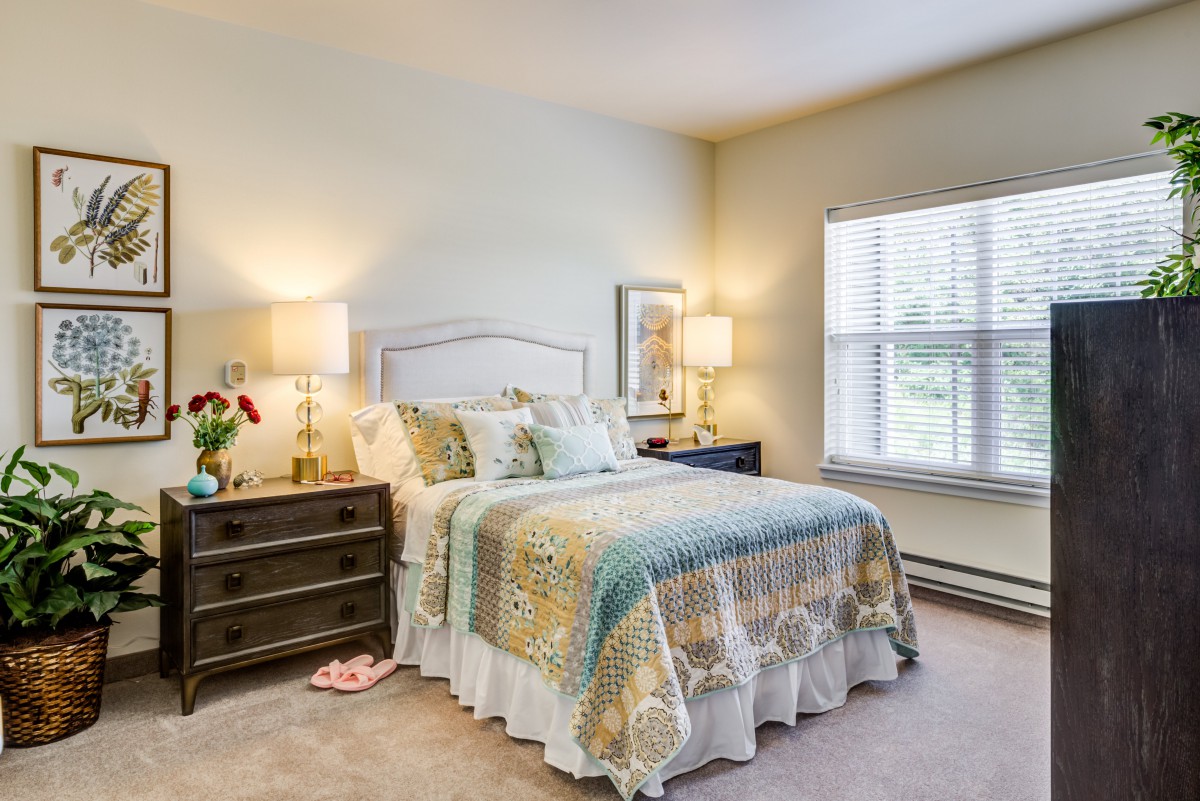 A cozy bedroom with a neatly made bed, two bedside lamps, and a window letting in natural light.