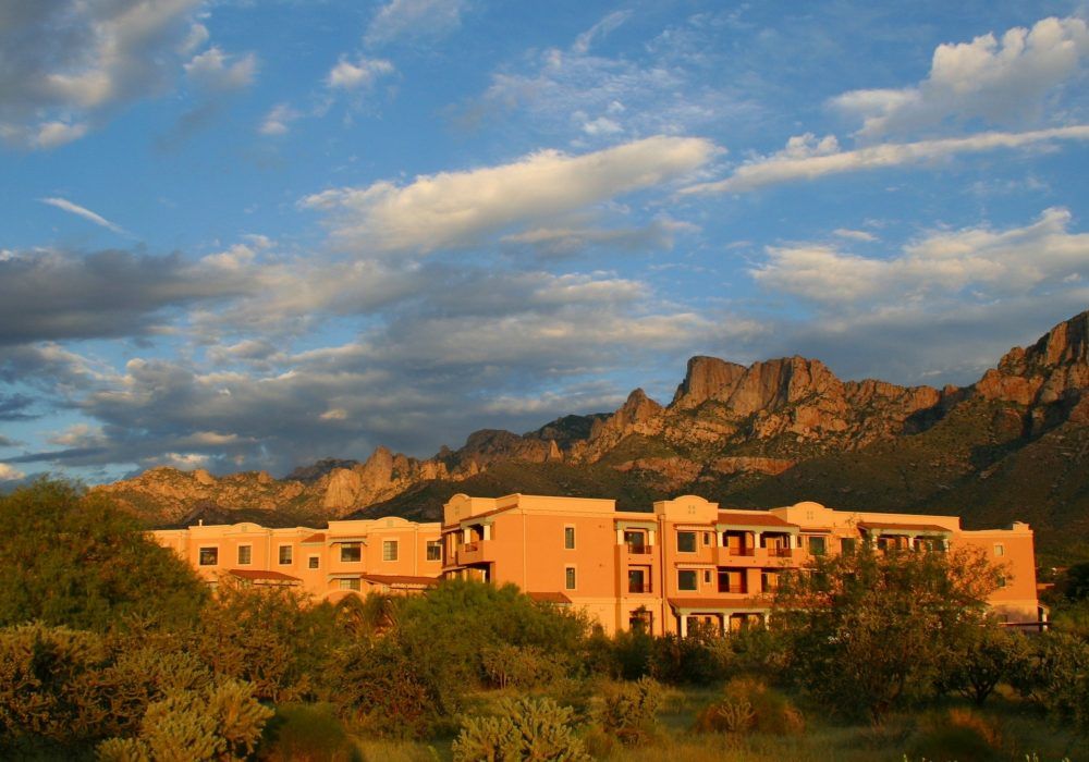 A resort building basking in the warm glow of a sunset, set against a backdrop of rugged mountains and desert landscape.