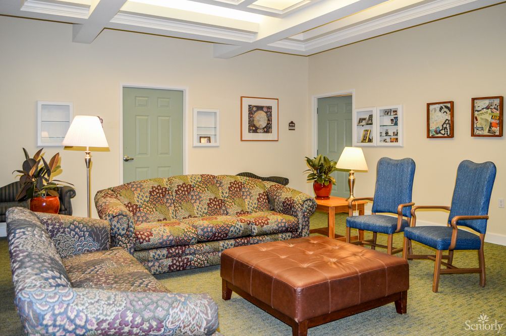 A cozy living room featuring a patterned sofa, armchair, and a large coffee table with lamps and plants for decoration.