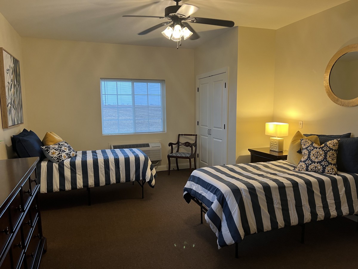 A cozy bedroom with two striped beds and a ceiling fan.
