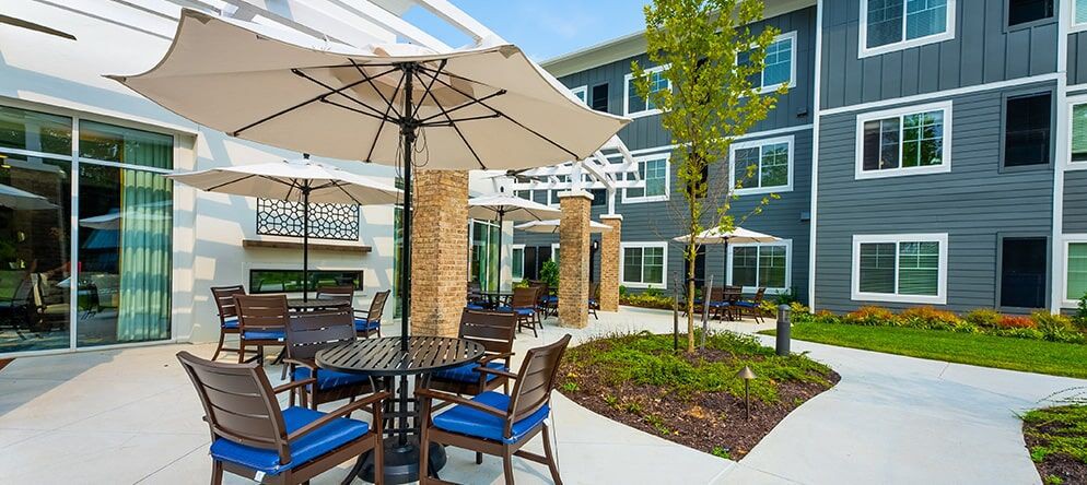 A modern outdoor patio area with tables, chairs, and umbrellas, surrounded by well-maintained landscaping.