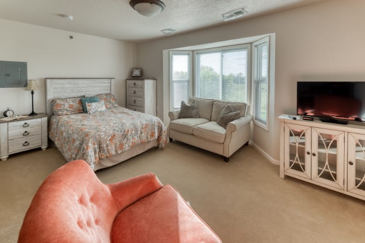 A cozy bedroom with a bed, sofa, armchair, and large window.