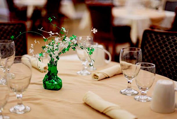 A beautifully arranged dining table with a floral centerpiece in a green vase, surrounded by glassware and neatly folded napkins.
