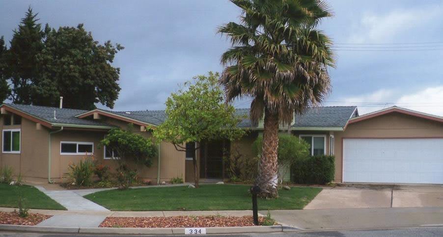 A suburban house with a palm tree and well-maintained lawn on an overcast day.