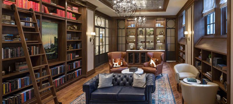 A luxurious library with elegant armchairs, a leather sofa, and well-stocked bookshelves under a grand chandelier.
