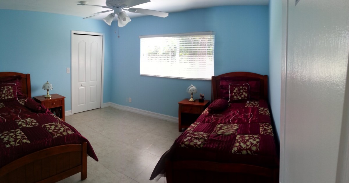 A bedroom with blue walls, featuring a single bed, nightstand, and ceiling fan.