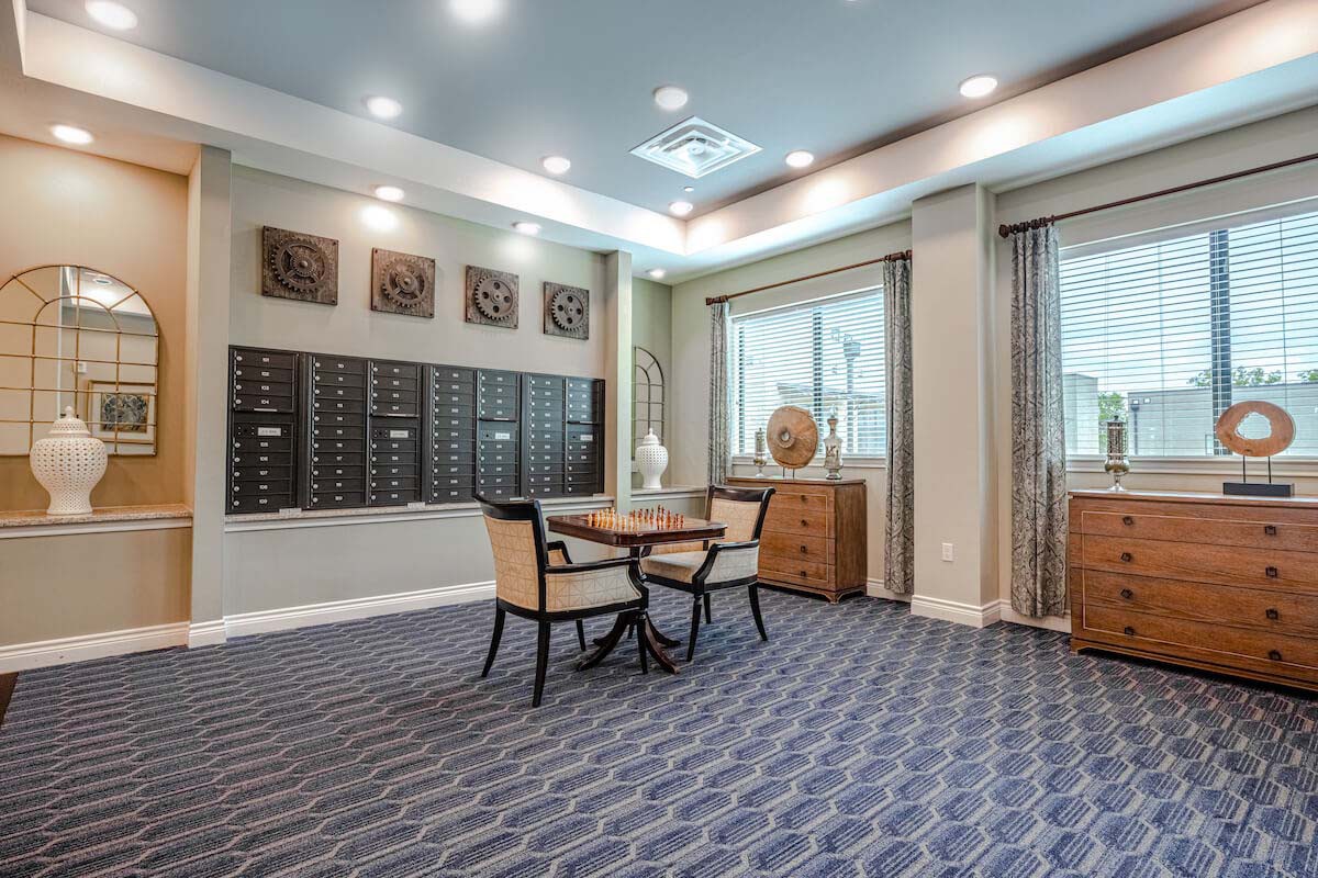 A modern lobby with a seating area, featuring a table and chairs, surrounded by mailboxes and large windows.