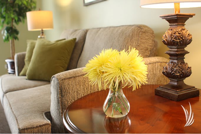 A cozy living room with a vase of yellow flowers on a wooden table next to a comfortable sofa.