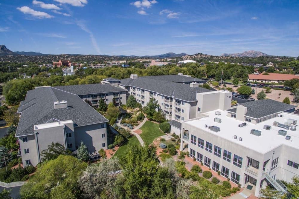 Aerial view of a complex surrounded by greenery and hills under a clear sky.