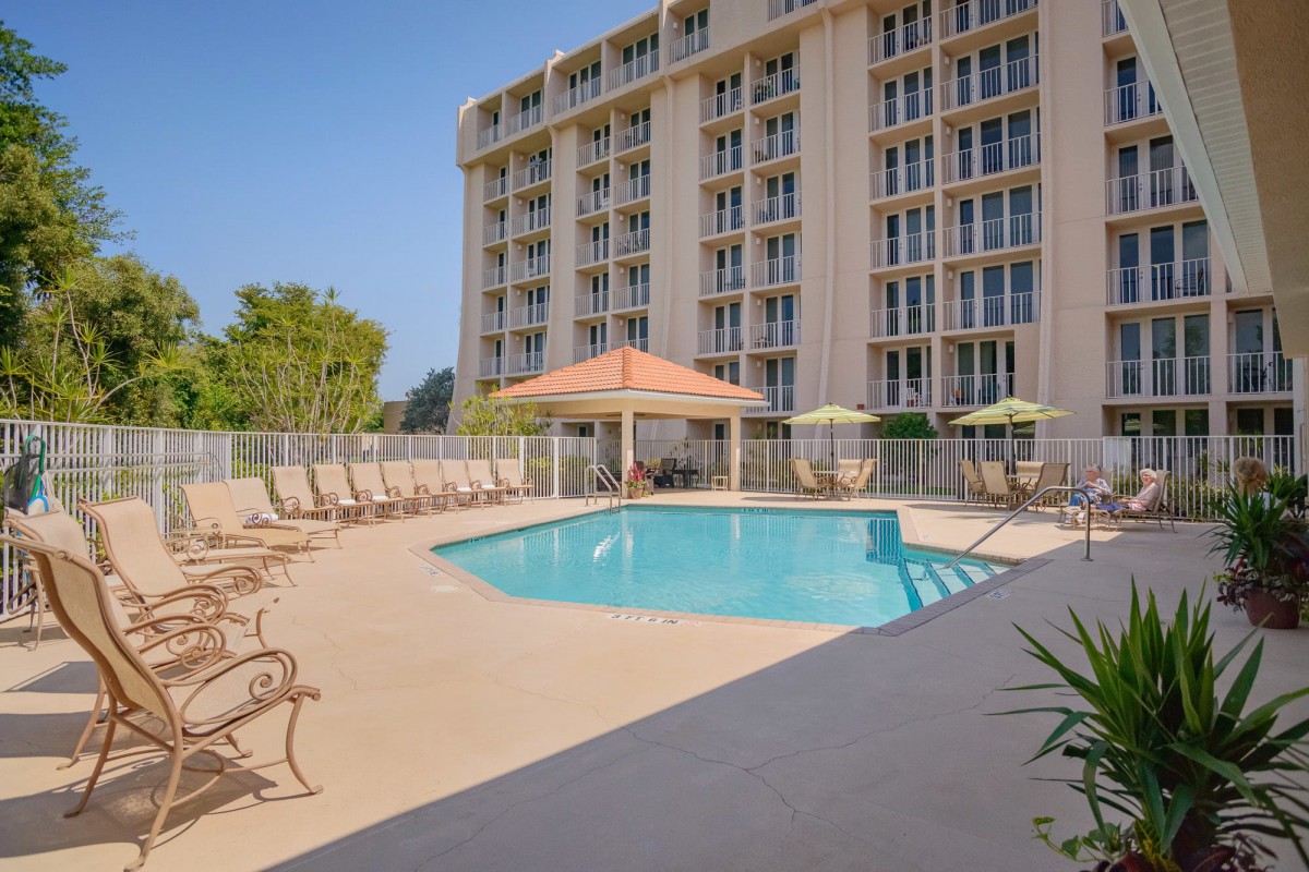 An outdoor swimming pool area with lounge chairs and a canopy beside a multi-story hotel building.