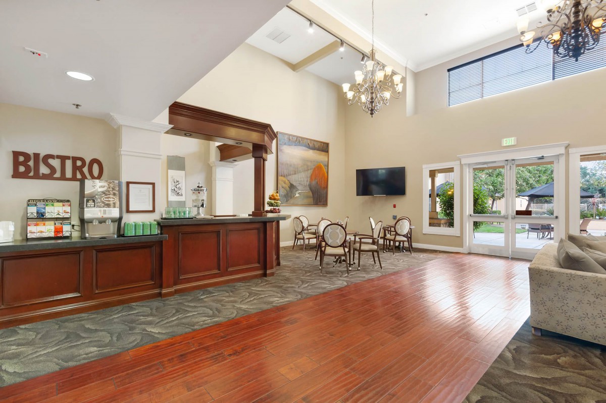 A spacious hotel lobby with a reception desk, chandelier, seating area, and wood flooring.