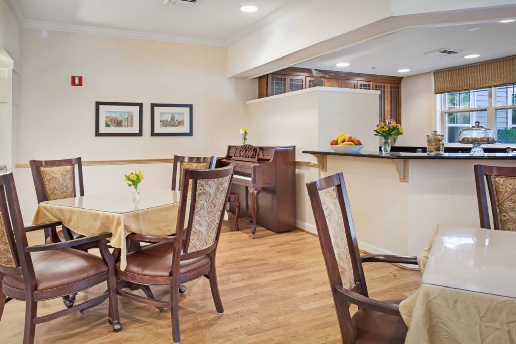 A cozy dining area with a piano, tables, and chairs on a wooden floor.