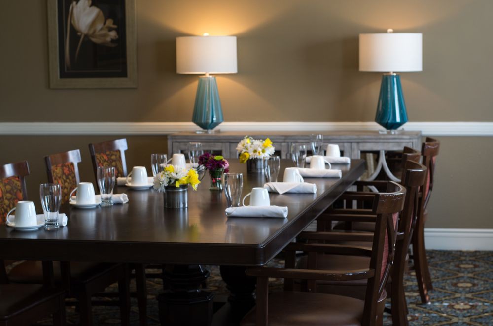 A dining room table elegantly set with flowers, surrounded by wooden chairs and illuminated by warm lamps.