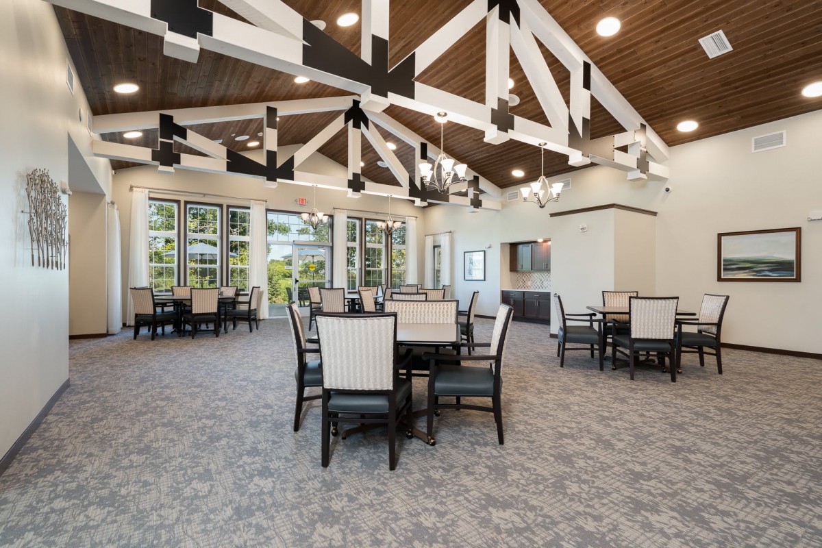 A modern dining area with tables and chairs, featuring large windows and exposed ceiling beams.