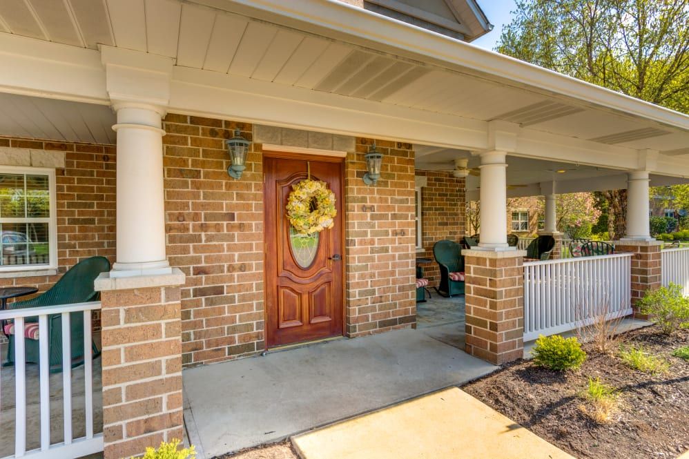 A welcoming front porch with brick walls, a wooden door adorned with a wreath, and comfortable outdoor seating.