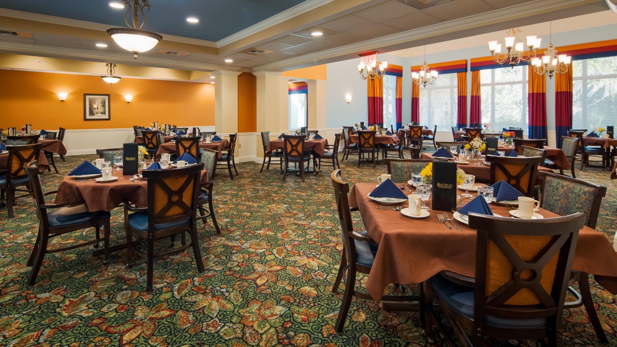 An elegant restaurant dining room with neatly arranged tables and chairs, featuring vibrant decor and warm lighting.
