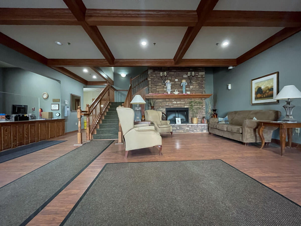 A cozy lobby interior featuring a seating area with sofas and armchairs, a fireplace, and wooden stairs.