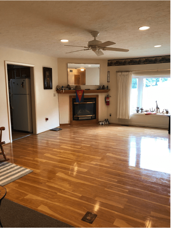 Spacious living room with hardwood flooring, a fireplace, ceiling fan, and a window seat.