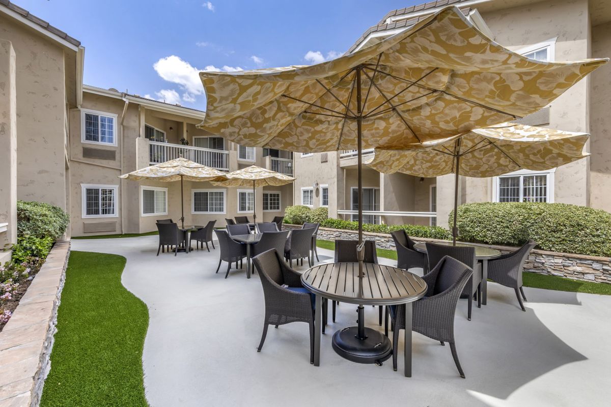 An inviting outdoor patio with tables, chairs, and umbrellas at an apartment complex.