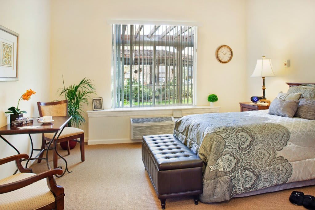 A well-furnished bedroom with a large window, featuring a bed, desk, and decorative elements.