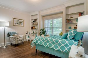 A cozy bedroom with a teal-themed decor, featuring a bed, shelves, and a large window.