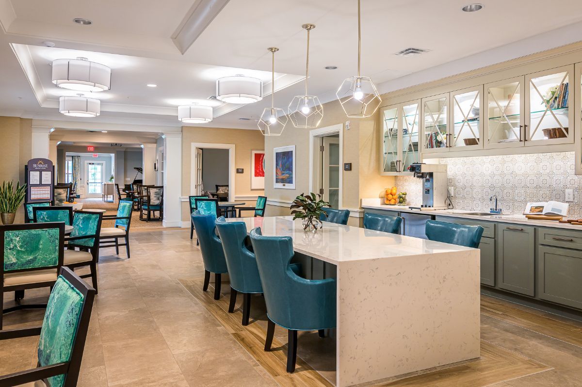 A modern dining and kitchen area with blue upholstered chairs and a sleek marble countertop, illuminated by chandelier lighting.