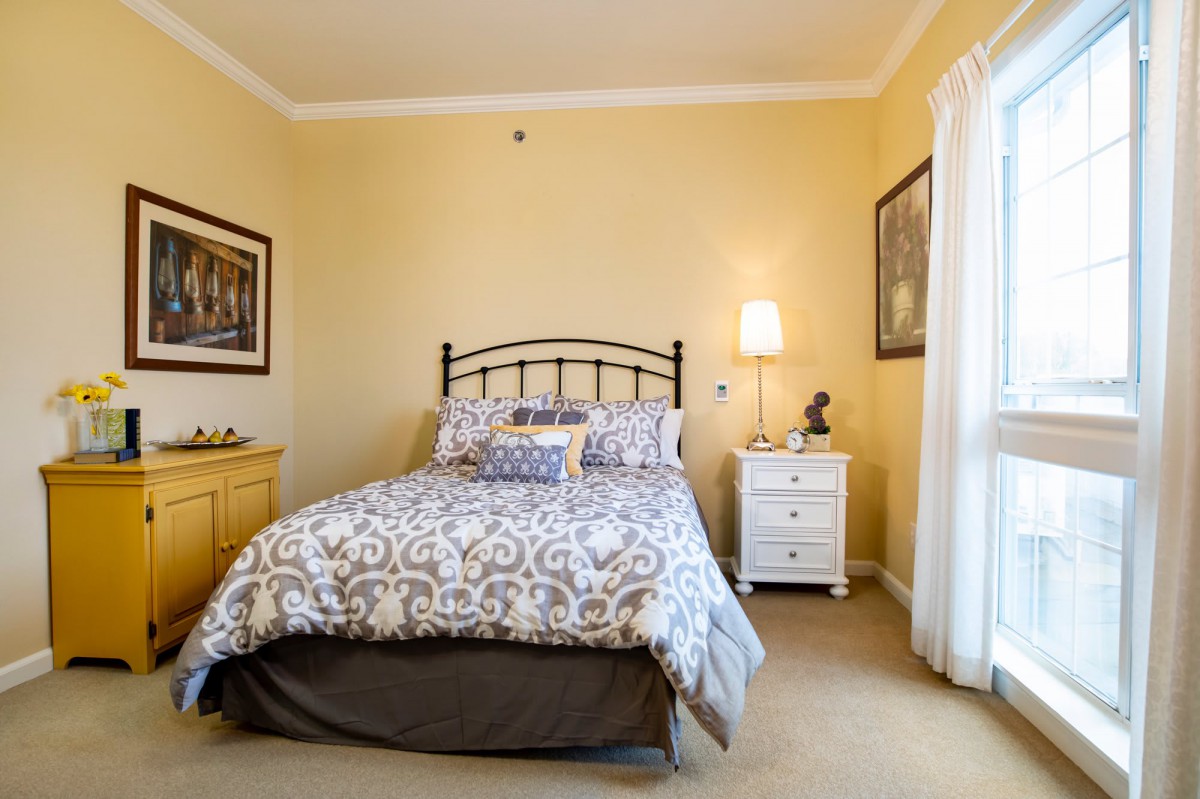 A cozy bedroom with a metal-framed bed, patterned bedding, and a nightstand with a lamp.