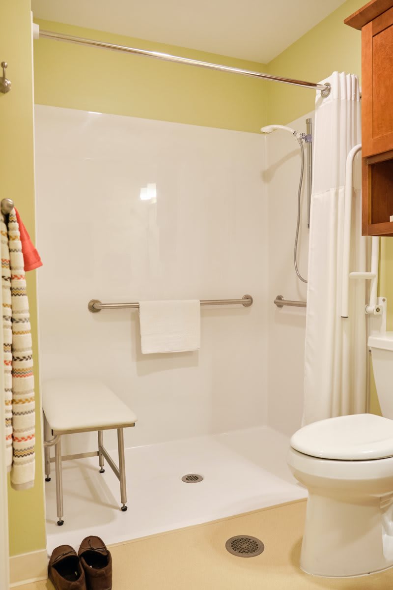 A bathroom featuring an accessible shower with grab bars and a bench.