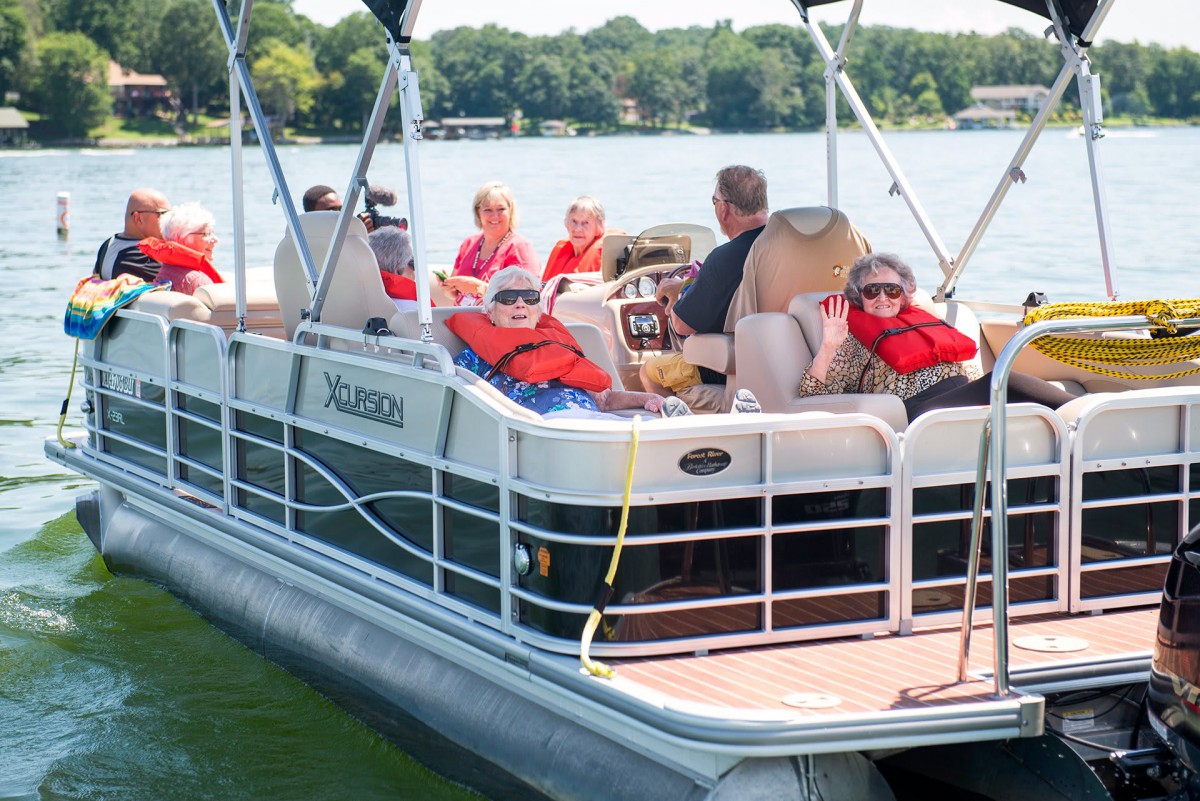 A group of people wearing life jackets relax on a pontoon boat on the lake during a sunny day.