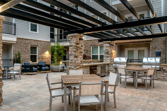 A modern outdoor patio with comfortable seating and a pergola, situated in an apartment complex.