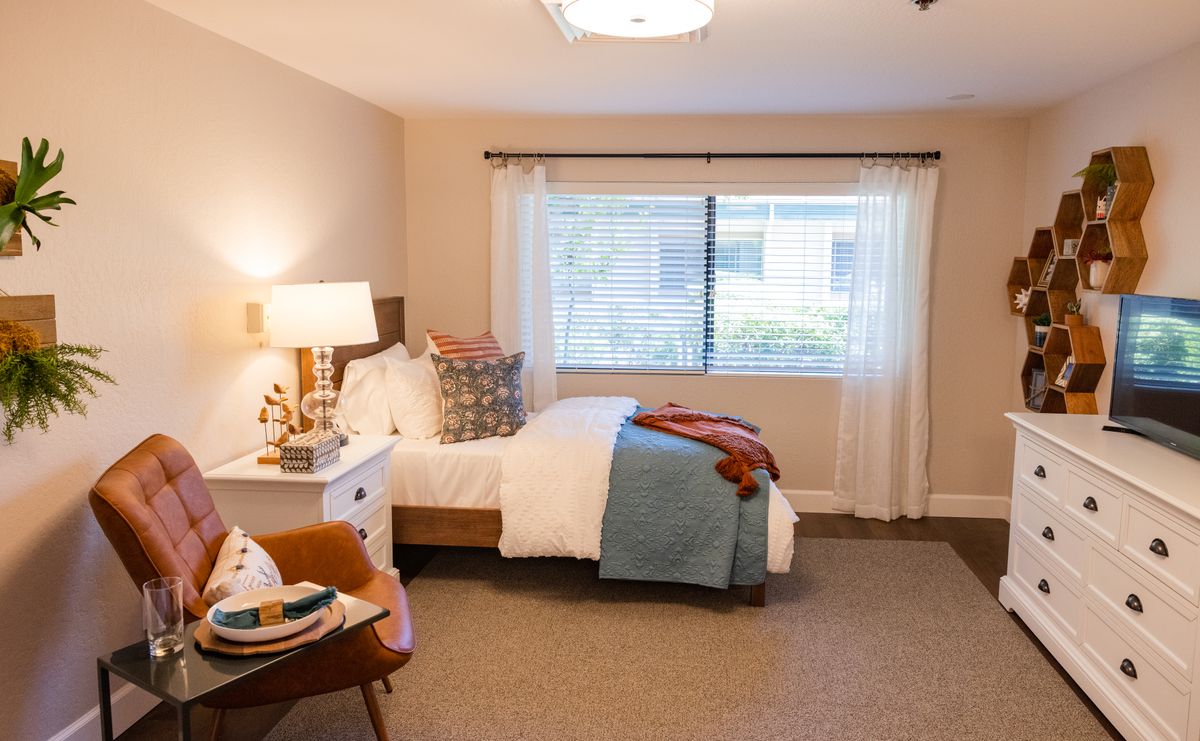 A cozy and well-decorated bedroom with a comfortable bed, an armchair, and natural light streaming through the window.