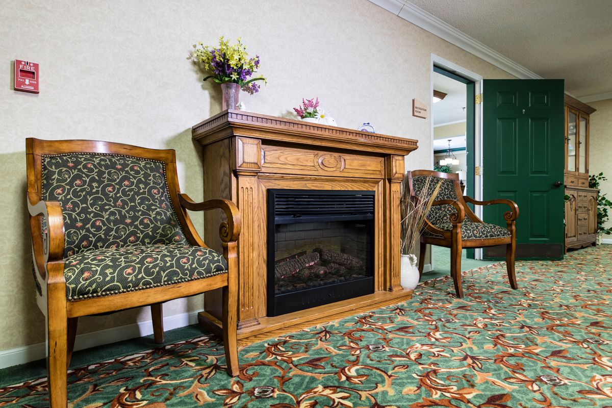 A cozy room featuring a wooden fireplace and elegant chairs on a patterned carpet.