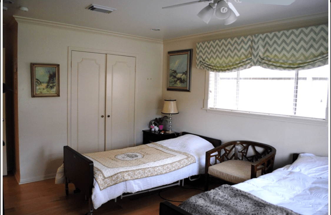 A cozy bedroom with a single bed, a window with patterned curtains, and various pieces of furniture.