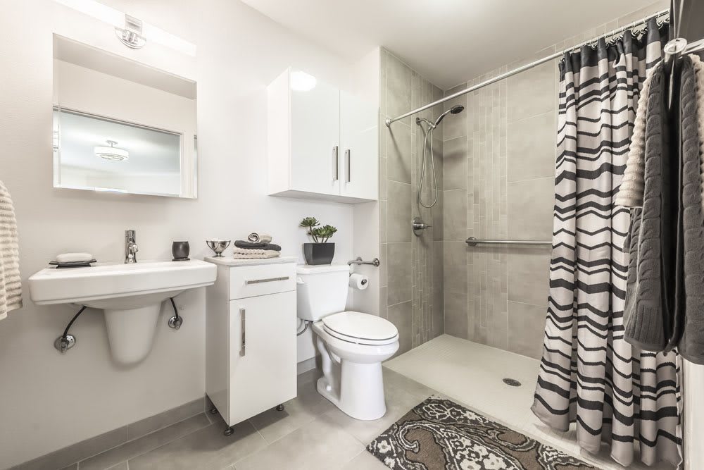A modern, minimalist bathroom with a white color scheme featuring a shower, toilet, and sink.