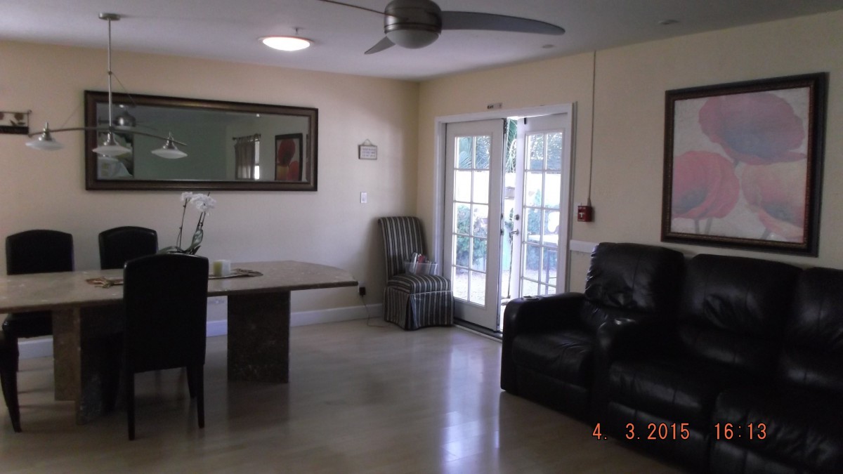 A living room with a table, chairs, and an armchair, featuring a mirror on the wall and a ceiling fan.